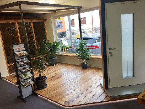 Moderner Ausstellungsraum mit Haustür, Holzfußboden, Prospektständer und grünen Pflanzen.